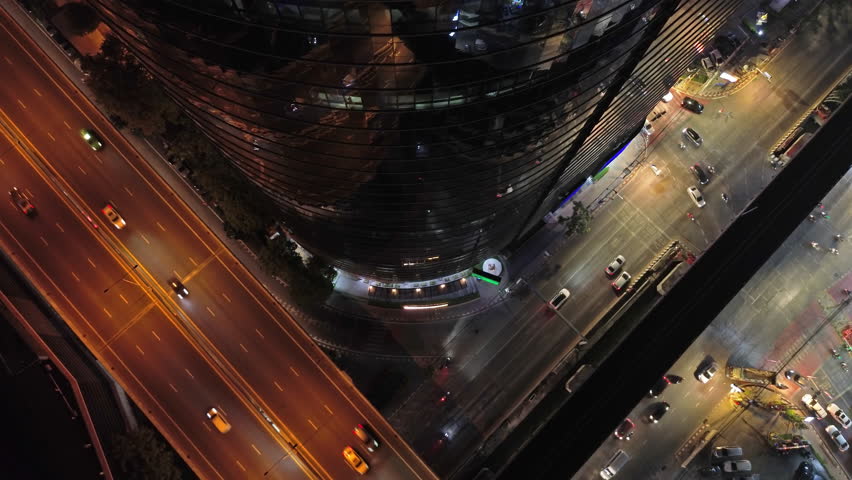 Aerial top view of skycrapper with reflection in glass busy traffic at night in big city, rush hour traffic, 4k