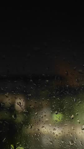 Rain. Drops on glass. Cose-up of rainfall. City at night. Streetlight. Bolts of lightning