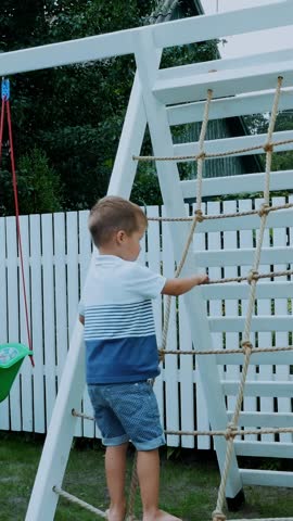 Child, a four year old boy climbs the children's stairs on the playground. The family spends their leisure time together.