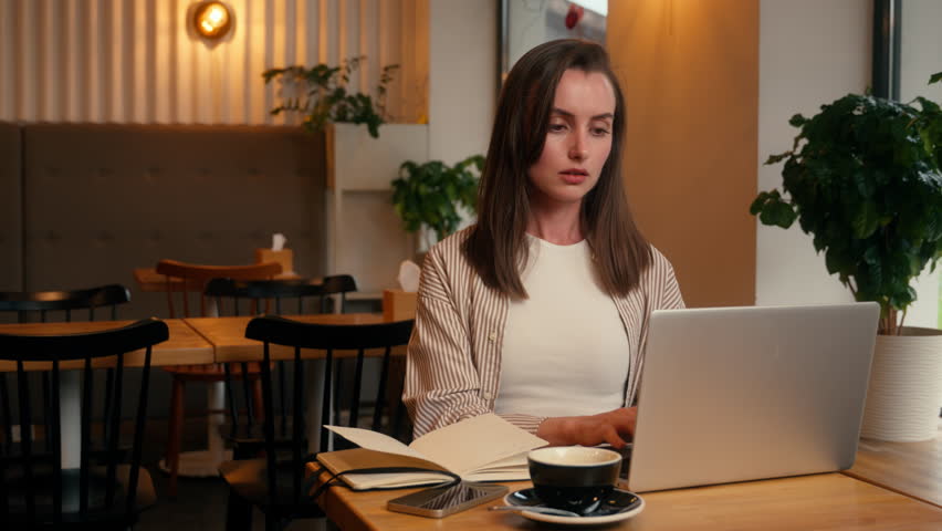 European woman concentrated busy in cafeteria manager analyzing data girl female studying in cafe remote write preparing to exams writing notes with laptop net working businesswoman business distant