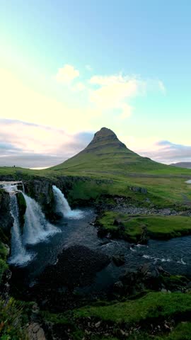 Experience the breathtaking beauty of Kirkjufell Mountain surrounded by lush greenery and cascading waterfalls. The tranquil environment showcases Icelands natural wonders at dusk.