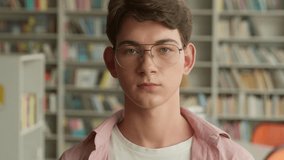 Portrait indoors in school library book store university college academy serious calm Caucasian student boy in glasses looking at camera gaze man male schoolboy guy education studying headshot frown - Powered by Shutterstock - Get 15% off with code: PIKWIZARD15
