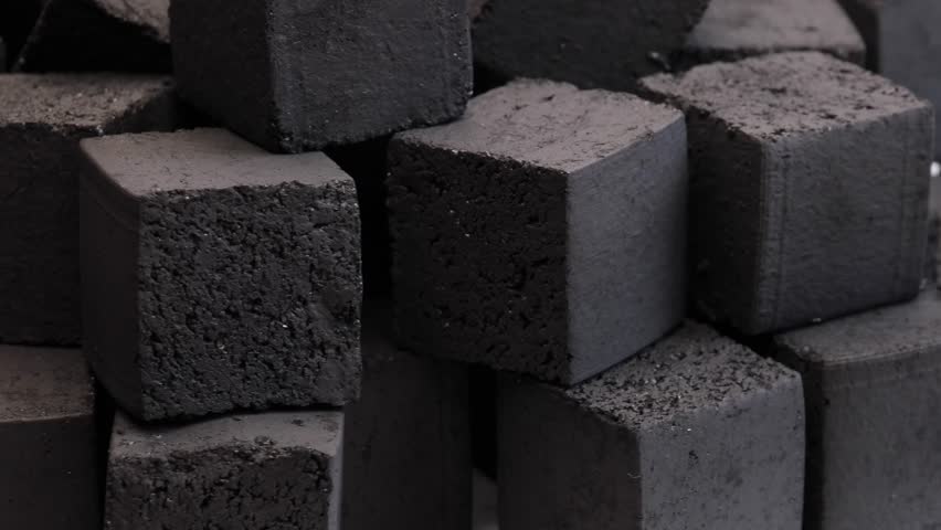 pile of pressed coal cubes for hookah stacked together on white background showing rough and smooth surfaces concept of hookah lounge tobacco shop smoking accessory