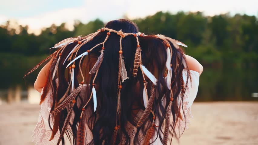 girl in white dress clothes bohemian style hands are adjusting touching hair long dark hair decorated headband with feathers stylish boho hippie. Woman summer enjoying freedom nature back rear view.
