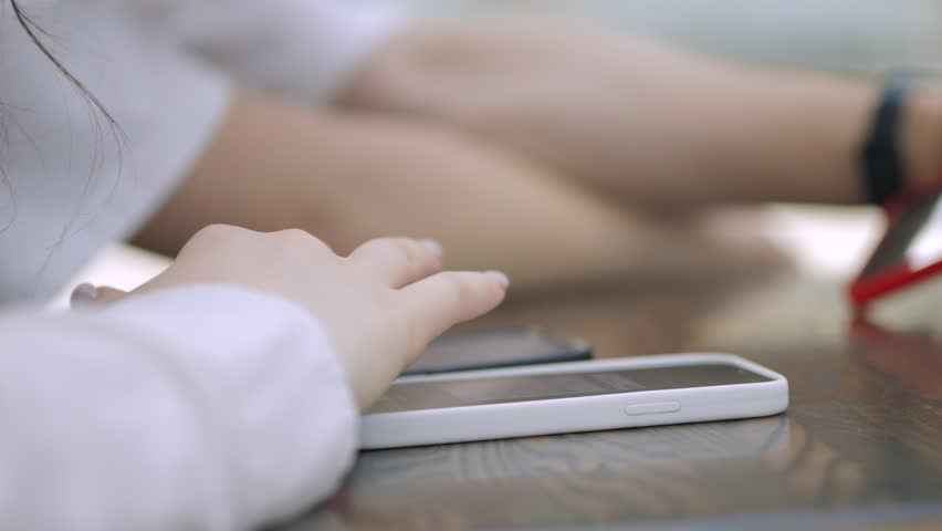 Woman is using her cell phone while sitting at a table. The table has a few other items on it, including a cell phone, a watch, and a pair of scissors. Concept of productivity and multitasking
