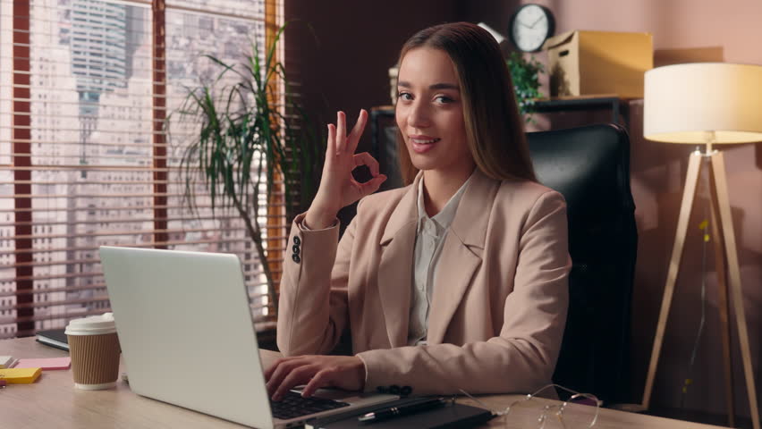 Happy cheerful smiling Caucasian woman female lady businesswoman office worker business person entrepreneur employee working laptop typing keyboard computer looking at camera show okay ok good indoors - Powered by Shutterstock - Get 15% off with code: PIKWIZARD15