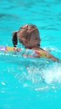 Happy little girl laughs and plays in blue hotel pool with rubber ring. Child fun swims and splashes with inflatable circle. Summer vacation holiday travel. Vertical shot - Powered by Shutterstock - Get 15% off with code: PIKWIZARD15