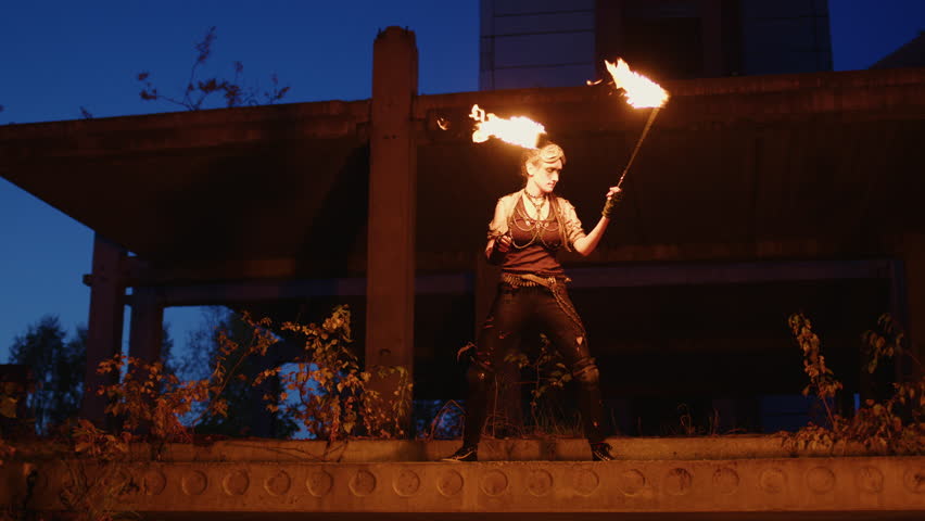 Fire dancer performing captivating skills with flaming torches, illuminating decaying architectural backdrop during twilight