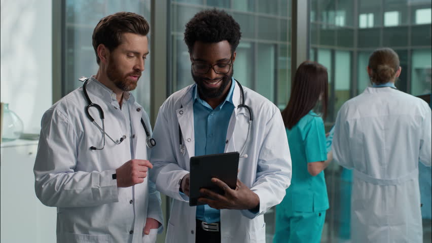 Two people men multiethnic doctors talking African American and Caucasian interns uniform labcoat discuss plan for recovery disease rehabilitation using digital tablet together teamwork at hospital