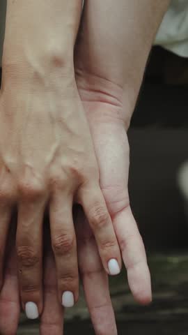 VERTICAL VIDEO Close-up shot of a couple in love holding hands, lovers gently stroking each other's hands, love, care, tenderness, slow motion. 