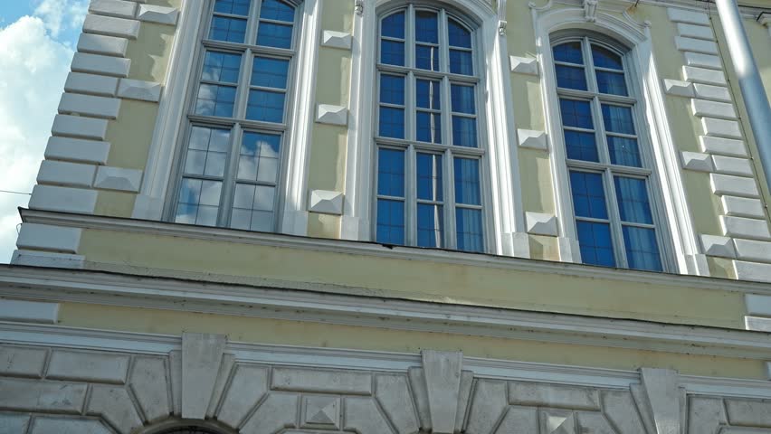 Detailed view of large arched windows and a historic clock on the facade of the town hall in Ingolstadt, Germany, under clear blue sky.
