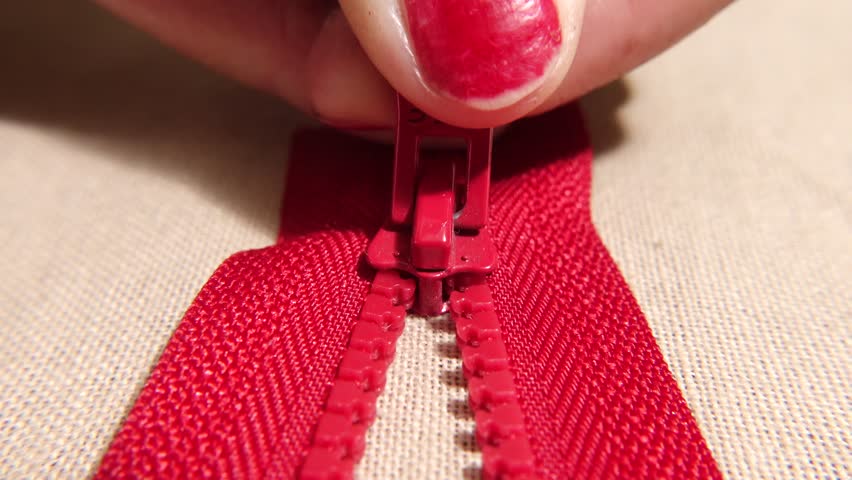 A macro shot showcasing a hand pulling a red zipper on beige fabric. The tailor is opening a zipper.
