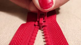 A macro shot showcasing a hand pulling a red zipper on beige fabric. The tailor is opening a zipper. - Powered by Shutterstock - Get 15% off with code: PIKWIZARD15
