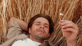 Man relaxing in golden wheat field while observing a delicate flower - Powered by Shutterstock - Get 15% off with code: PIKWIZARD15