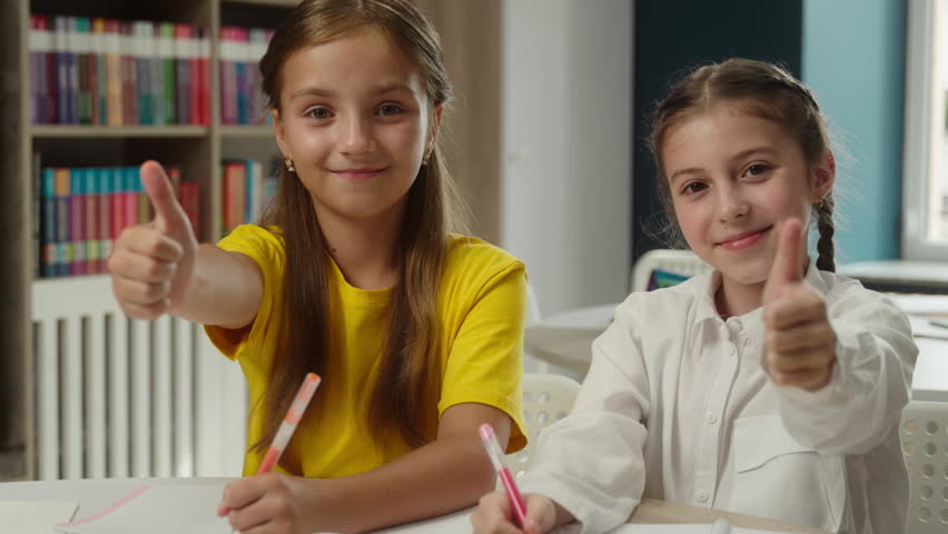 Little girls children Caucasian schoolgirls pupils friends sisters teen kids primary school education two students studying together classroom homework smiling thumbs up gesture recommend study learn - Powered by Shutterstock - Get 15% off with code: PIKWIZARD15