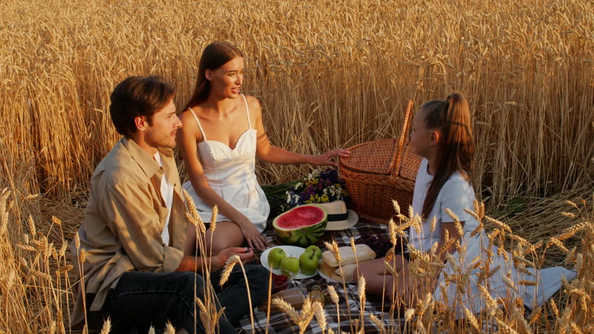 Family enjoy a picnic in a golden wheat field during sunset