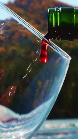 Enjoy the soothing experience of red wine being poured into a glass, capturing the essence of autumn with colorful leaves in the background. Perfect for relaxing moments.