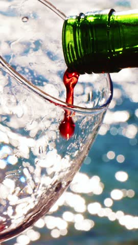 A beautiful stream of red wine fills a clear glass amid sparkling reflections on the water. Enjoying this moment evokes relaxation and warmth as the sun shines brightly.
