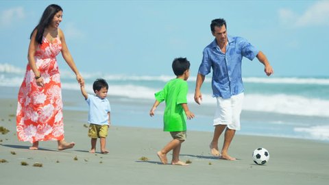 Latin American young loving parents walking on beach playing football with children shot on RED EPIC
