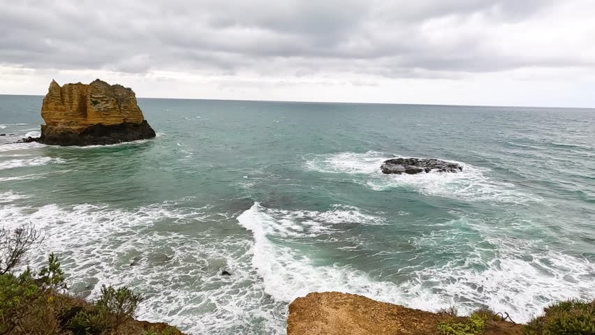 Ocean waves crash against a solitary rock formation under cloudy skies along the Great Ocean Road in Australia