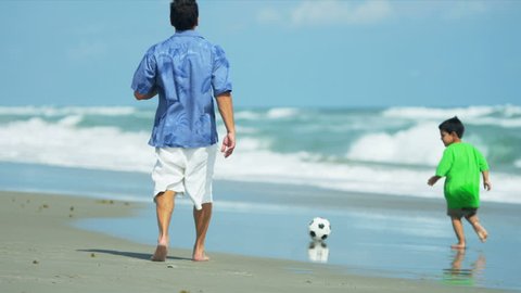 Hispanic loving father kicking ball with young son on beach shot on RED EPIC
