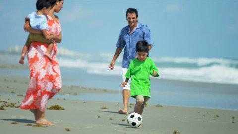 Latin American father enjoying kicking ball with young little kid on beach shot on RED EPIC