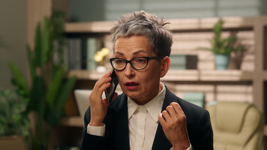 Angry stressed yelling talking mobile phone old middle-aged European business woman mature female dissatisfied employer businesswoman in office talk arguing smartphone conflict corporate quarrel bad