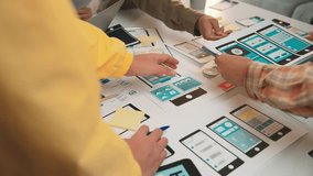 A dynamic scene showcasing hands of designers as they collaborate on mobile and web application wireframe prototypes, surrounded by sketches and notes in a creative workspace. SACTR - Powered by Shutterstock - Get 15% off with code: PIKWIZARD15