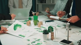 A diverse team discusses sustainable strategies during a business meeting, surrounded by documents, green models, and digital tools to drive eco-friendly initiatives. SACTR - Powered by Shutterstock - Get 15% off with code: PIKWIZARD15