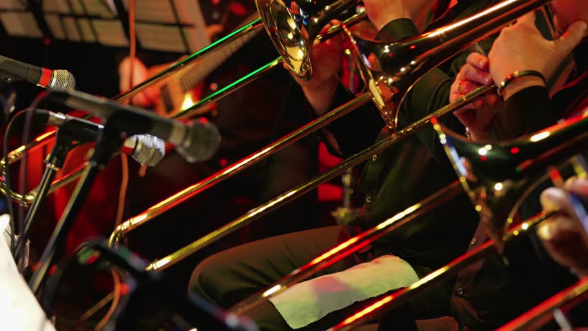 A vibrant jazz scene featuring musicians playing trombones. Microphones capture the lively atmosphere. Close-up of the trombone section