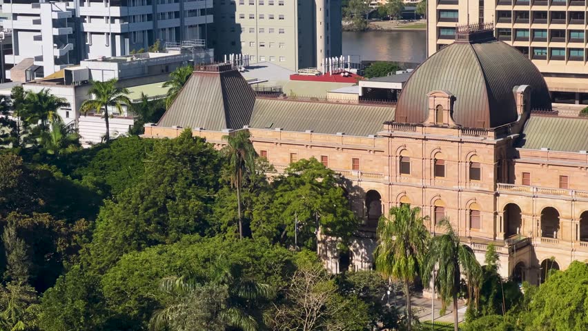 Old sandstone Queensland Parliament building with trees and modern buildings around