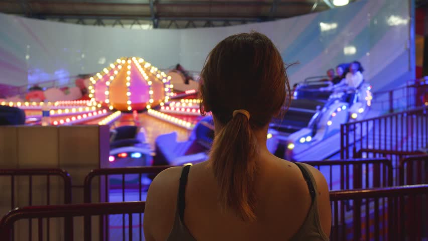 Colorful night scene featuring woman with ponytail observing spinning carnival ride, glowing landscape embodying festive atmosphere and youthful exuberance