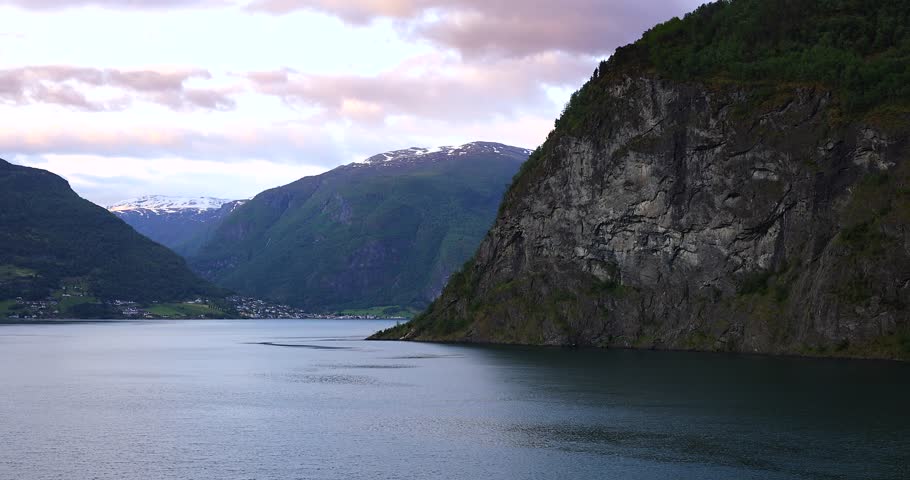 Majestic green cliffs and deep blue fjord waters under clear skies, filmed from a cruise ship sailing through the breathtaking landscapes of Norway fjords.