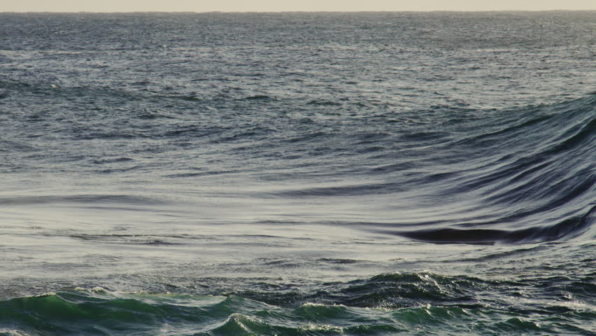 Slow motion capture of rising wave in side profile, white crest and rippling deep ocean below