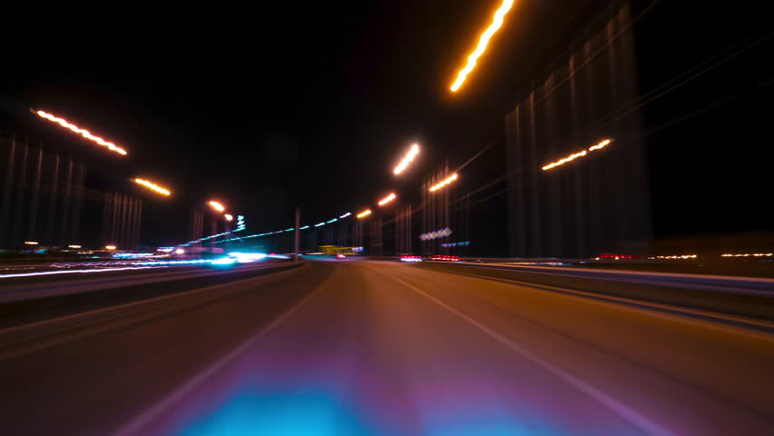A Car Speeds Down the City Highway. Chaotic Lights Blur Into Bright Streaks. The Simulation of High-speed Movement Captures the Rhythm of the City. Trip Travel Concept. 4K Point of View Hyperlapse