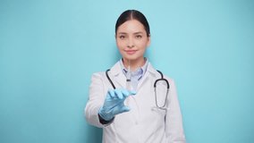 Smiling female doctor in white lab coat and gloves poised with medical syringe, representing vaccination or medical treatment, against light blue background - Powered by Shutterstock - Get 15% off with code: PIKWIZARD15