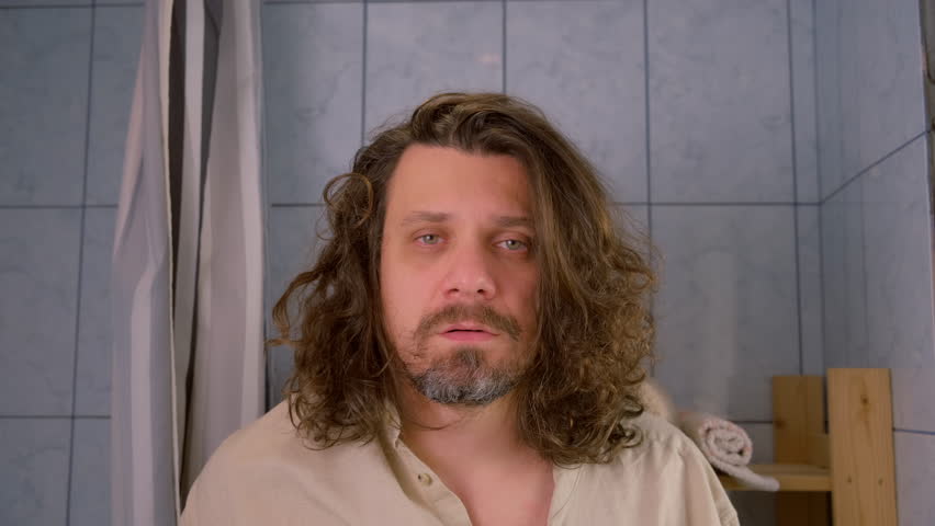 Long haired bearded man shocked his reflection in mirror in bathroom in morning. Lack of sleep, insomnia, stressful lifestyle, sleep deprivation. Changing depressive manic phrase of bipolar disorder.