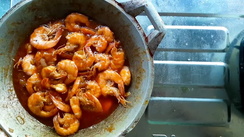 Top view of spicy Padang-style shrimp dish being cooked in a traditional wok. Indonesian cuisine featuring prawns in sweet, sour, and spicy sauce in a home kitchen