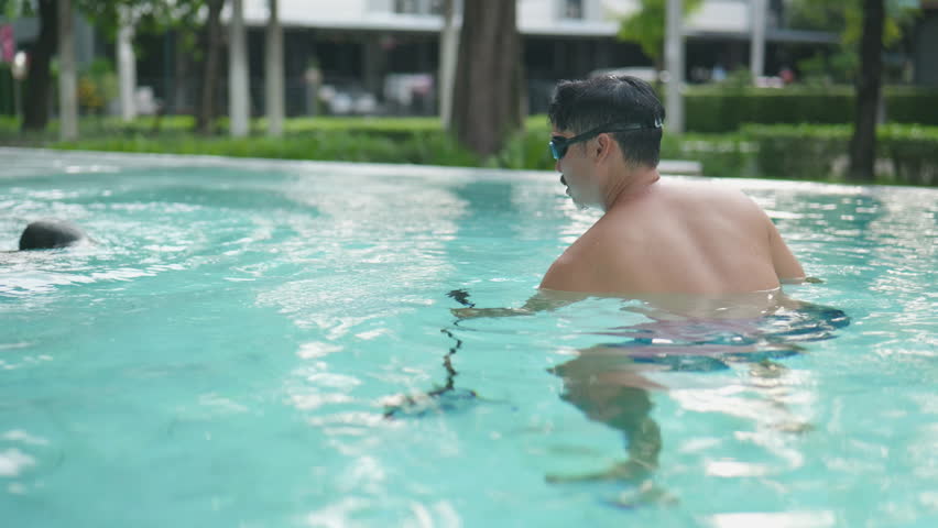 Asian boy dives toward his father in the swimming pool during a joyful holiday.4k