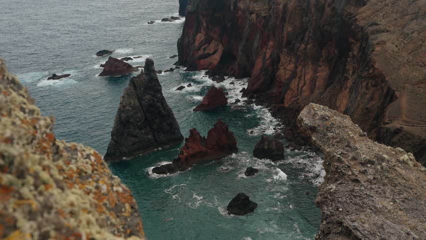 Jagged volcanic sea stacks rise from the Atlantic along Madeira’s rugged cliffs, framed by weathered rock.