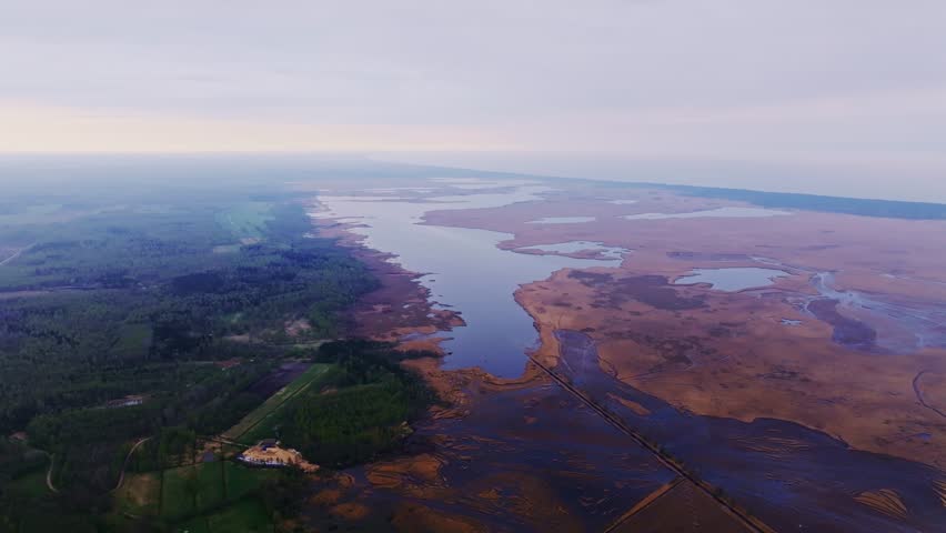 Sweeping drone, Latvia’s Pape Lake, winding shoreline and wetlands, spring haze