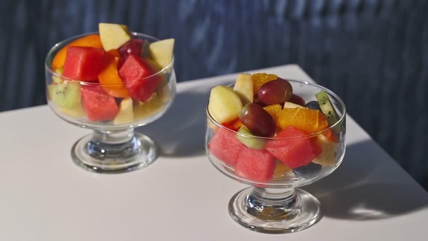bowl of fresh fruit salad on blue background and hand with fork, food closeup, healthy eating