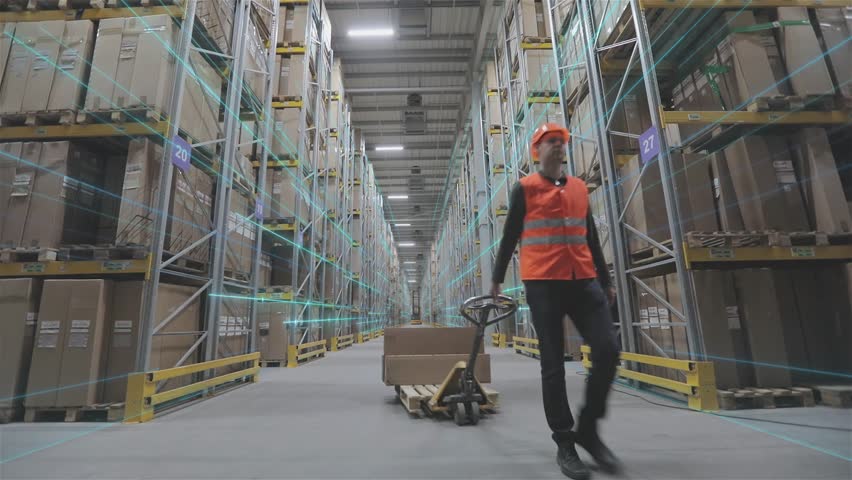 A warehouse worker is carrying cardboard boxes of products through the warehouse. Warehouse accounting and product picking. Working in a large modern multi-level smart warehouse inside