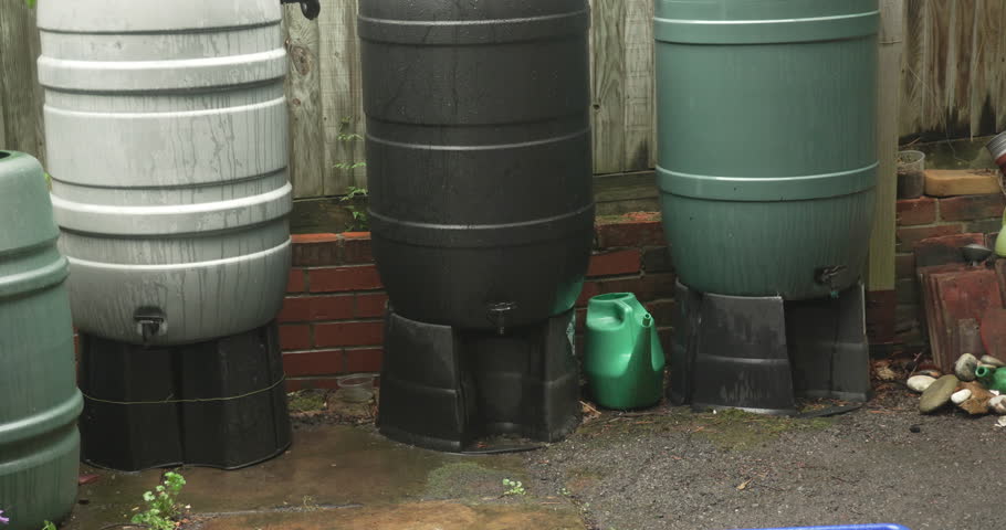 Three water barrels or butts linked storing harvesting rain water, ecology, sustainability, environment. Camera tilts up slowly.