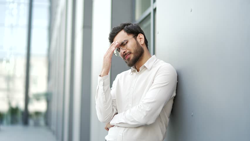 Upset businessman has depression suffering from mental pain while standing on the street near office building. Sad male has personal problems, worries, feels despair, disappointment, worries, stress