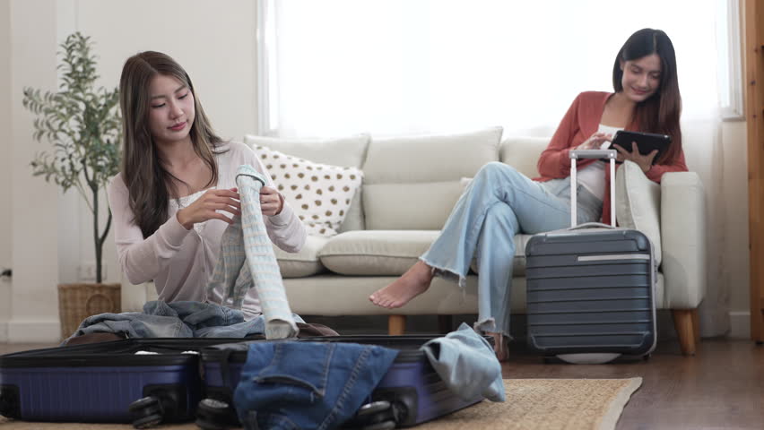 Young asian woman and friend preparing luggage packing clothes in suitcases for travel at home, planning holiday travel, content creator and travel blogger, friendship moments lifestyle vacation trip