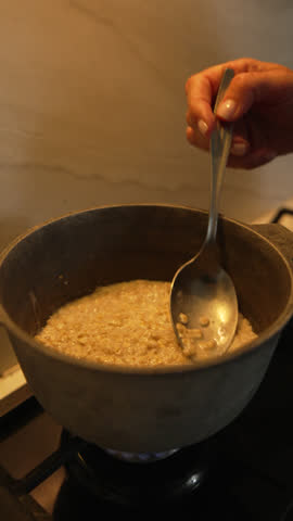 Spoon Stirring Pot Cooking - A hand stirs a pot of cooking food on a stove.