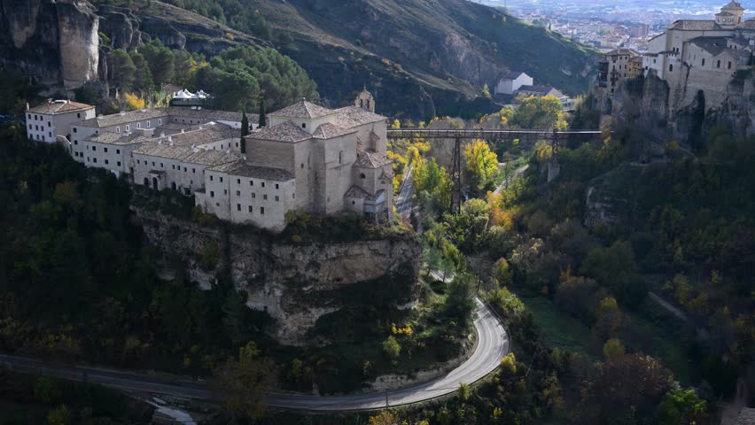 Vibrant autumn foliage colors the landscape around the historic city of Cuenca, Spain, framing the Parador hotel and the iconic Hanging Houses on the cliffs.