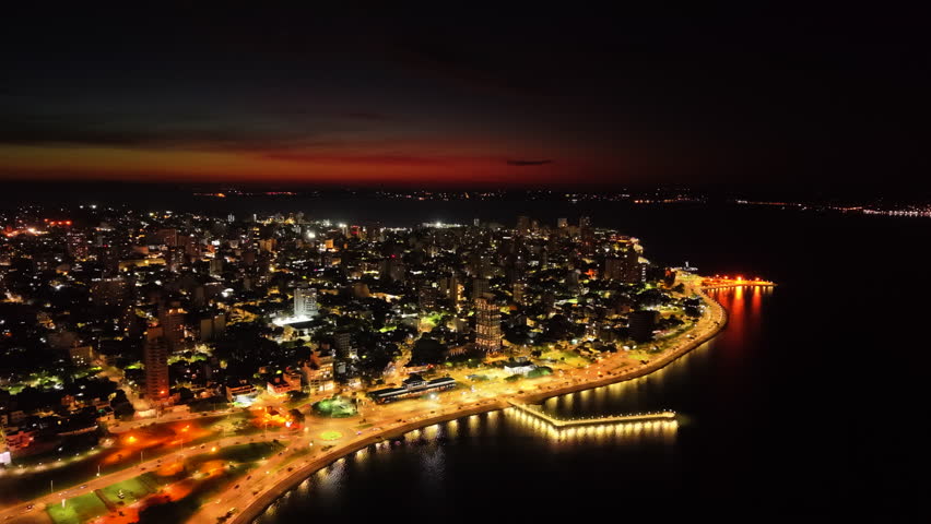 Dramatic aerial night view of lit coastline with beautiful urban light trails at the city of Posadas, Misiones, Argentina.