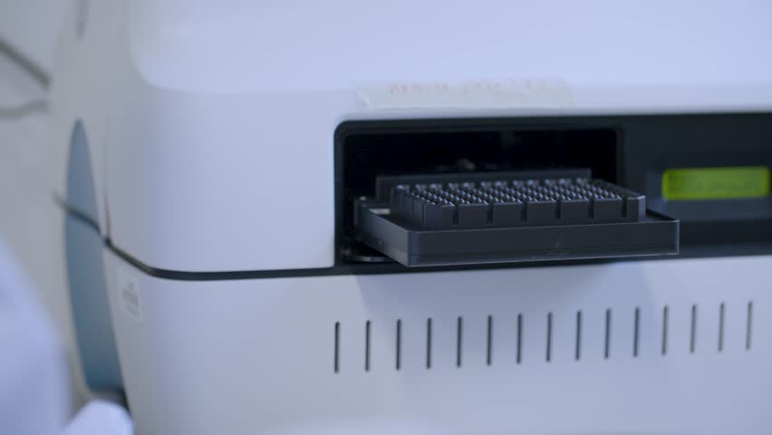 Close-up of automated lab equipment inserting a microtiter plate into a device for processing and scientific evaluation. Used in biology, chemistry, or pharmaceutical research.